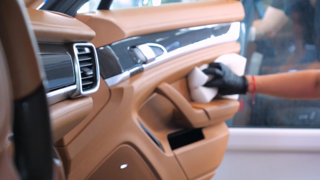 Autotür aus Leder wird von Hand mit Tuch gereinigt, professionelle Innenraumpflege mit Handschuhen