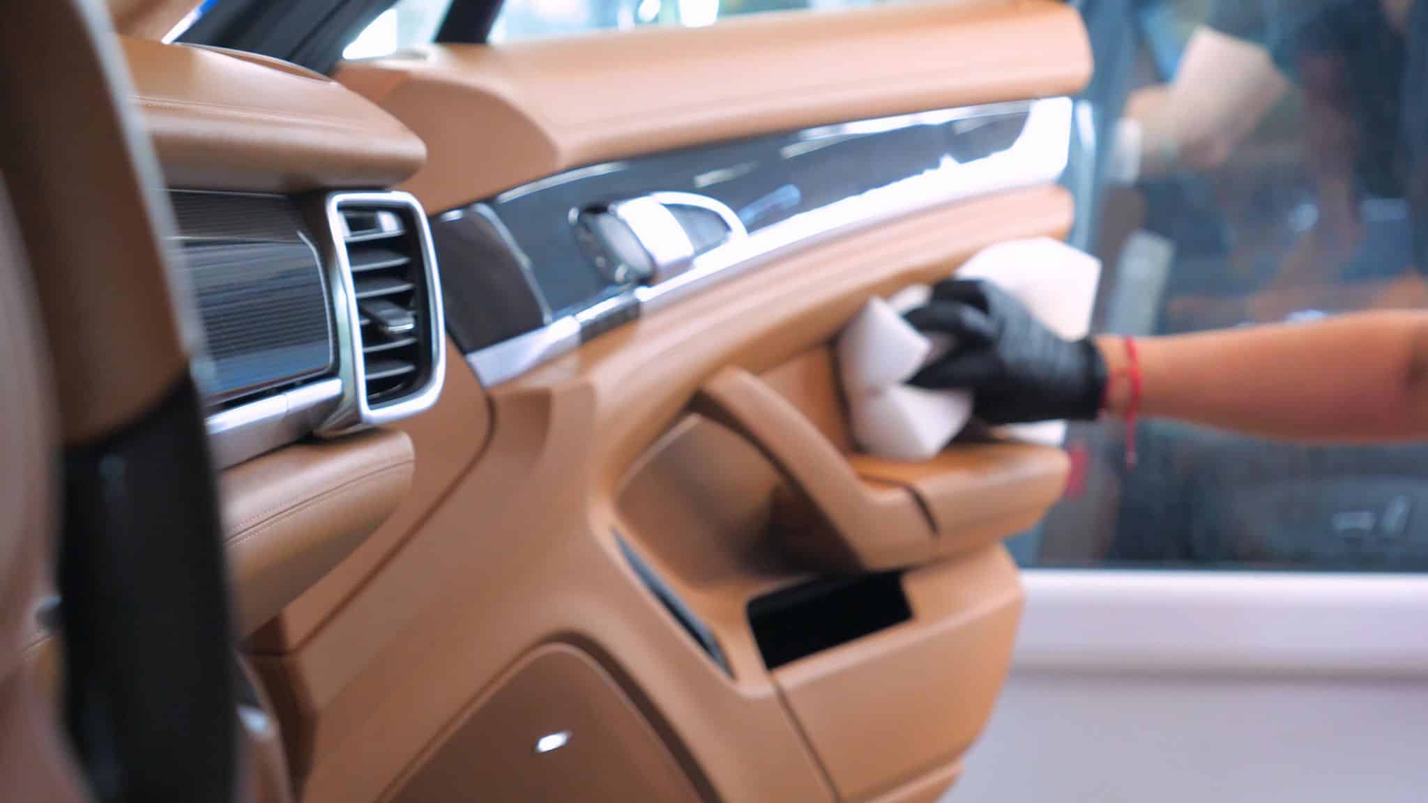 Autotür aus Leder wird von Hand mit Tuch gereinigt, professionelle Innenraumpflege mit Handschuhen