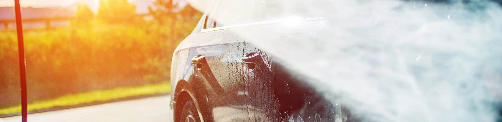 Fahrzeug wird bei Sonnenlicht mit Hochdruckreiniger gereinigt, Nahaufnahme einer professionellen Außenwäsche